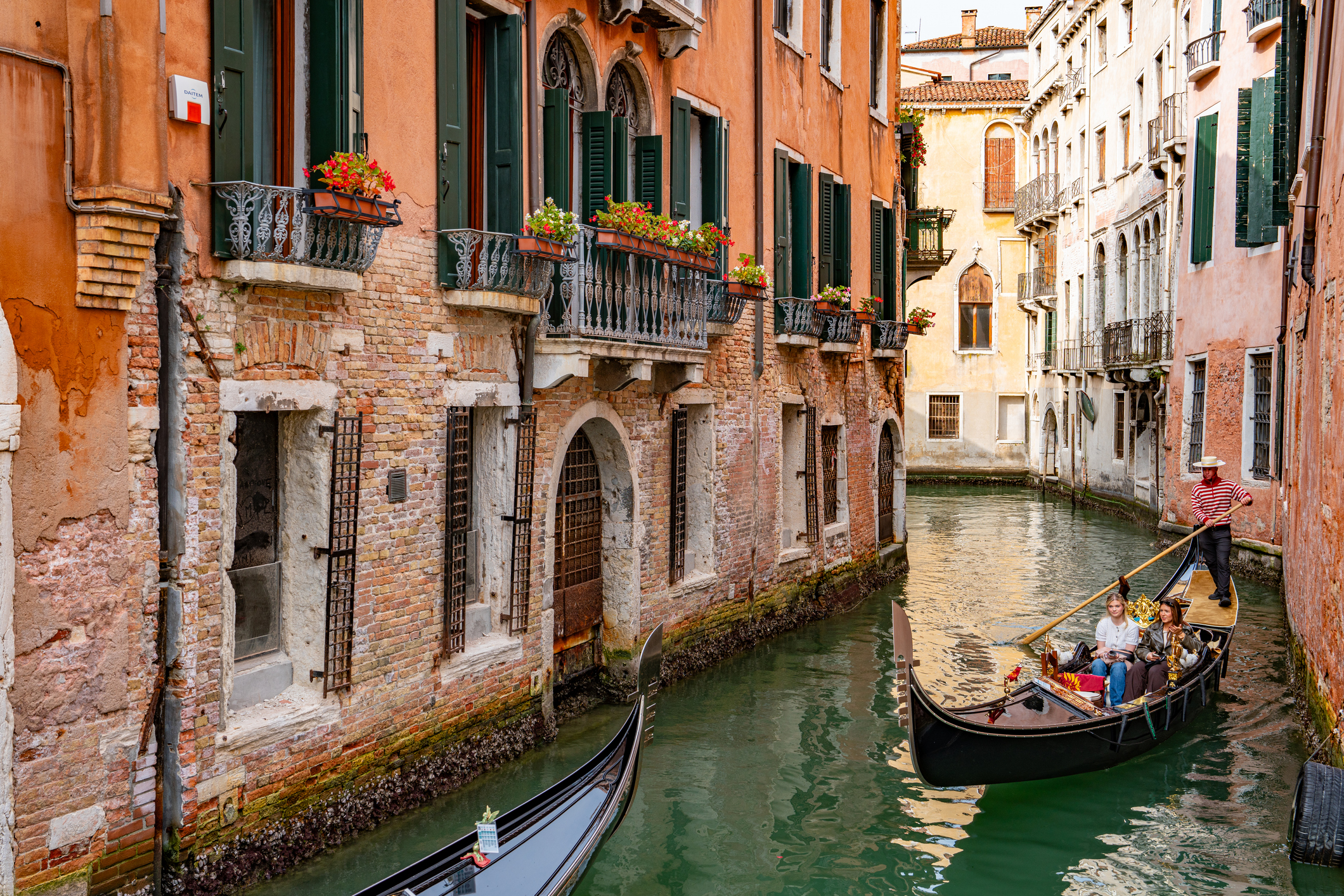 A classic black private gondola gliding through a quiet, romantic side canal in Venice at sunset